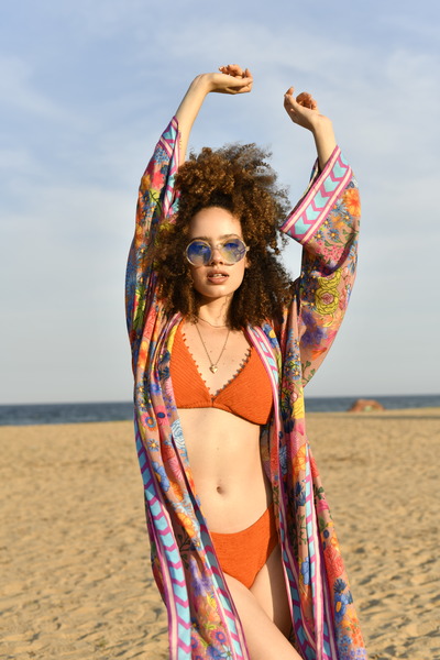 model wearing a rust colour bikini and a printed cover up with her hands up