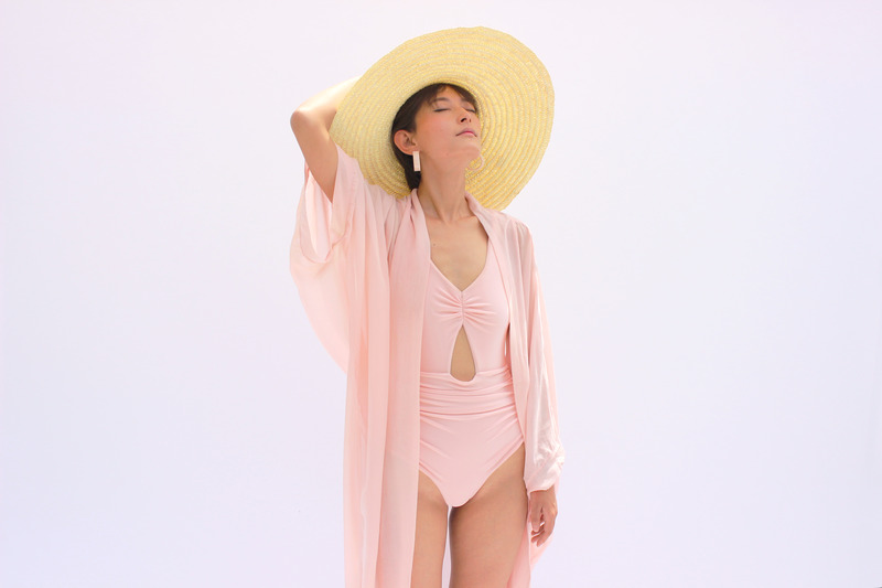 model wearing a baby pink one piece swimsuit with a coverup and a straw hat